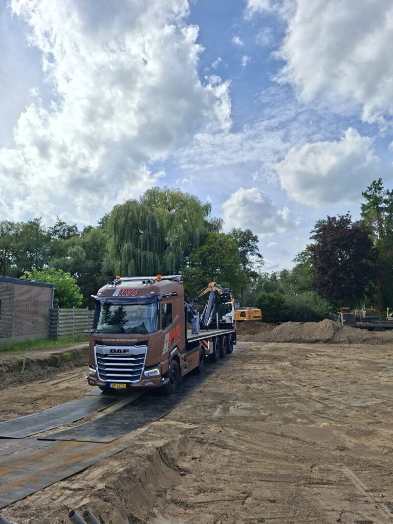 Vrachtwagen van RVS Rijplaten op rijplaten over de zandgrond van de bouwplaats in Voorst