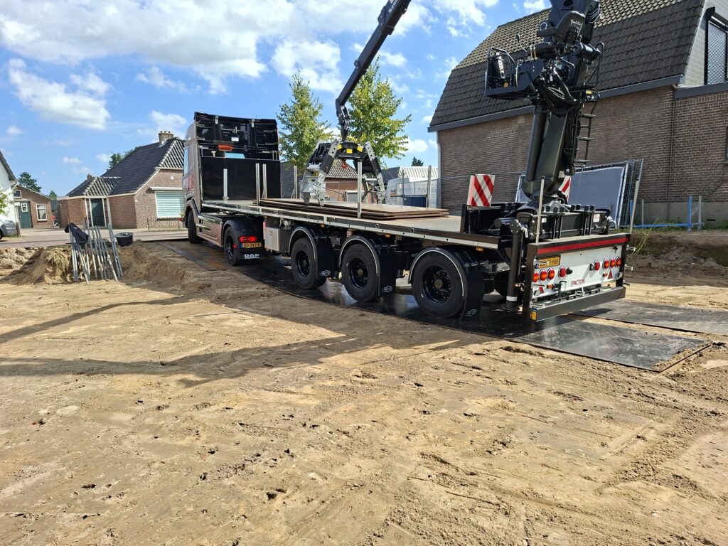 Kraanwagen lost stalen rijplaten op de bouwplaats van de appartementen in Voorst
